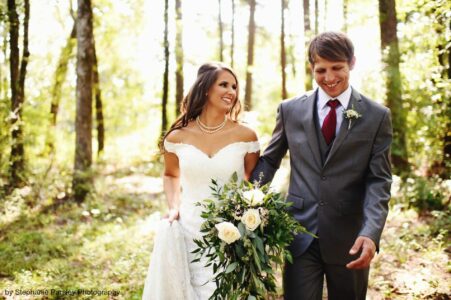 A bride and groom walking through the woods.