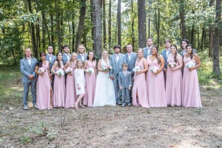 A group of bridesmaids and groomsmen posing for a photo in the woods.
